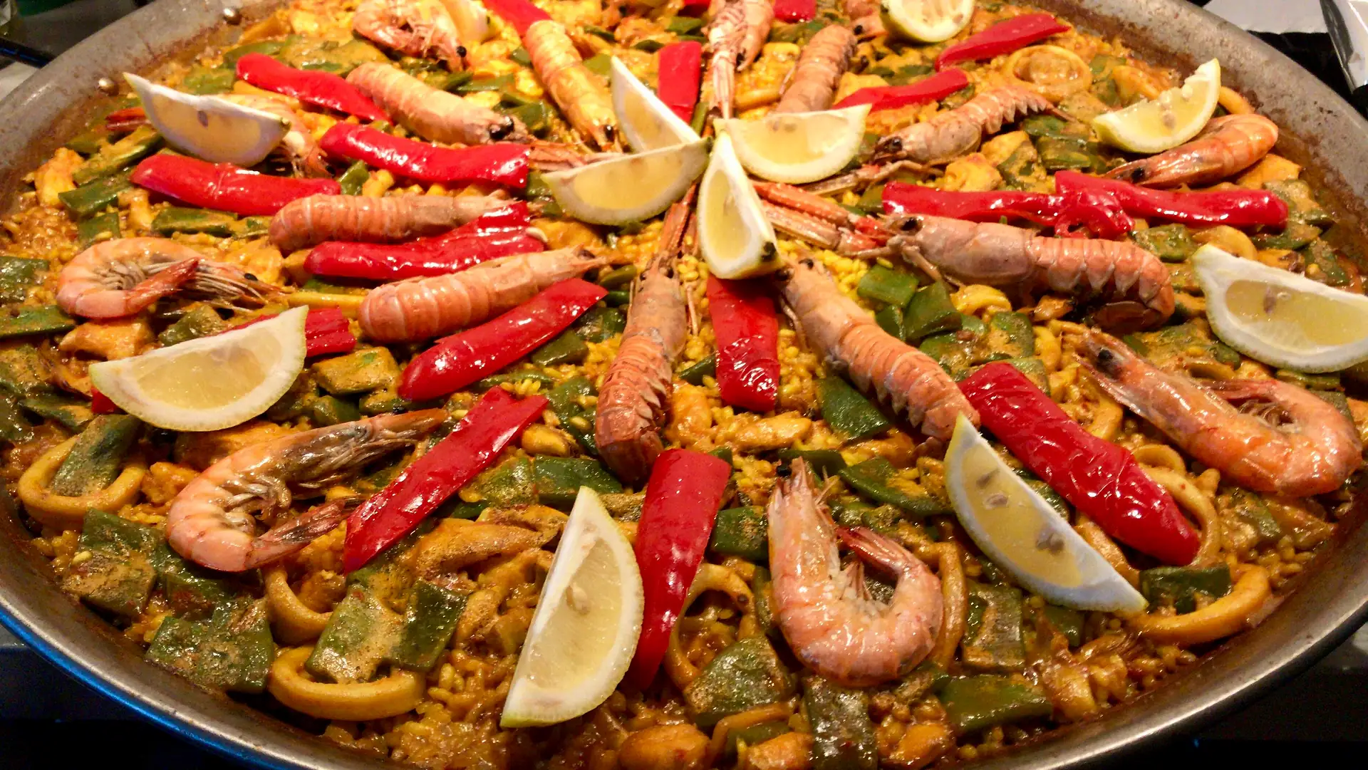 Paella de marisco recién hecha en su paellera, con langostinos, gambas, pimiento rojo y limón